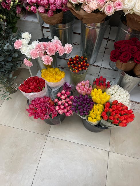 An assortment of fresh flowers arranged for a floral gift at a florist shop. The display includes various bouquets of tulips, carnations, and roses in vibrant colors such as red, pink, yellow, purple,