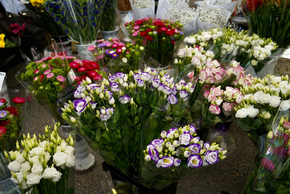 A vibrant display of fresh floral arrangements featuring a variety of flowers including purple and white eustoma, pink and white carnations, white lisianthus, and other colorful blooms. The flowers ar