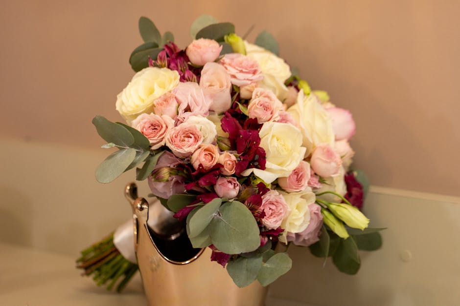 A bouquet arrangement featuring a mix of fresh flowers including pale pink roses, white roses, and deep burgundy blooms, complemented by green eucalyptus leaves. The flowers are tightly arranged in a